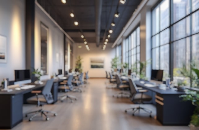 Modern open-plan office background with desks, monitors, and large windows with natural light